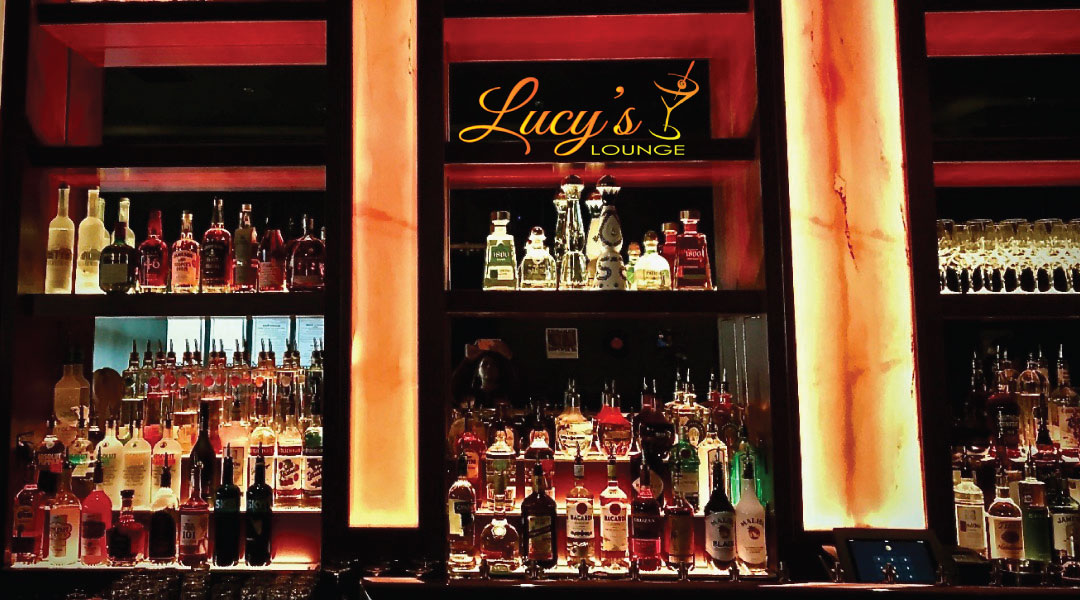 The back bar at Lucy's Lounge: shelves of bottles between glowing amber columns, under the Lucy's Lounge sign